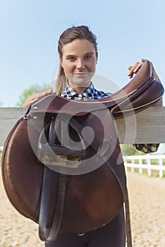 Female Horse Owner Standing With Leather Saddles Hanging On The Wooden Fence