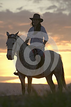 Female horseback rider and horse ride to overlook at Lewa Wildlife Conservancy in North Kenya, Africa at sunset