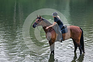 Female horseback rider riding a horse along the river at sunset