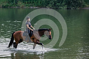 Female horseback rider riding a horse along the river at sunset