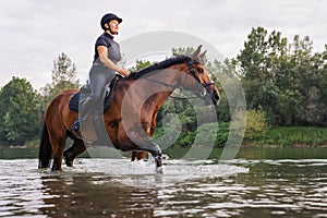 Female horseback rider riding a horse along the river at sunset