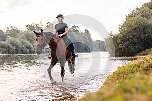 Female horseback rider riding a horse along the river at sunset