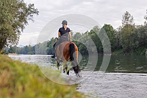 Female horseback rider riding a horse along the river at sunset