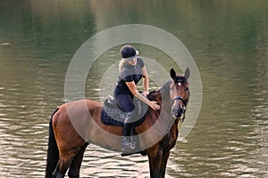Female horseback rider riding a horse along the river at sunset