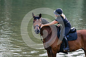 Female horseback rider riding a horse along the river at sunset