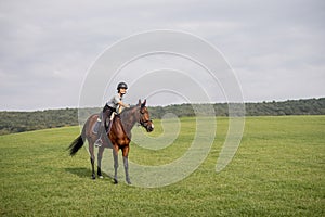 Female horseman riding brown Thoroughbred horse in meadow