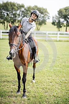 Female horseman riding brown Thoroughbred horse in summer