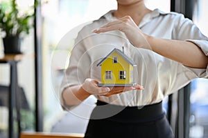 Female house insurance agent holding a yellow house model. house protection