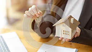 Female house insurance broker or real estate agent holding house key and house model