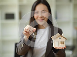 Female house realtor or real estate agent holding house keys chain and house model