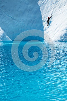 Female ice climber over deep blue water of the Matanuska Glacier