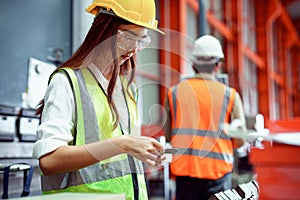 Female industrial engineer wearing a Yellow helmet while standing in a heavy industrial factory behind she Check with workers,