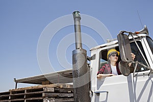 Female industrial worker adjusting mirror while sitting in logging truck