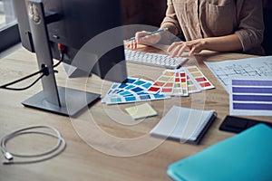 Female interior designer working on project of architecture drawing with color swatches, using computer at workplace