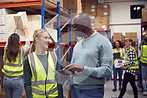 Female Intern With Team Leader Looking At Digital Tablet Inside Busy Warehouse Facility