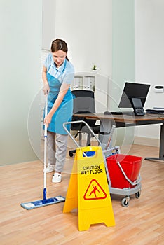 Female Janitor Cleaning Hardwood Floor In Office