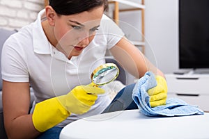 Female Janitor Examine Table Using Magnifying Glass