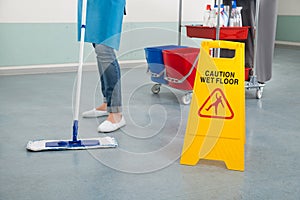 Female Janitor Mopping Corridor With Caution Sign