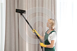 Female janitor removing dust from curtain