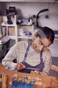 Female Jeweller At Bench Working On Ring With File In Studio