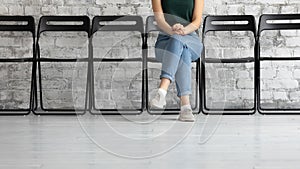 Female job applicant sitting on chair in corridor, cropped view