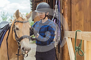 Female Jockey Fixing Bridle Of Her Light Brown Horse Outside The Stable