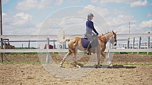 Female Jockey Wearing Helmet Riding On A Palomino Horse In The Sandy Arena