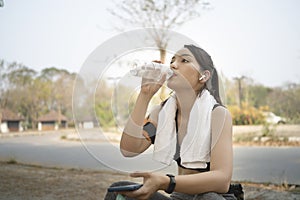 Female jogger drinking fresh water from plastic bottle after running on the park.