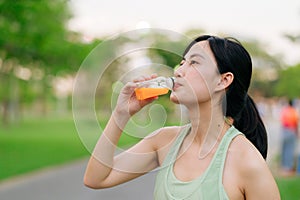 Female jogger. Fit young Asian woman with green sportswear drinking organic orange juice after running and enjoying a healthy