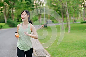Female jogger. Fit young Asian woman with green sportswear drinking organic orange juice after running and enjoying a healthy