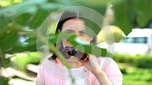 Female journalist with binoculars hiding behind trees, searching for sensation