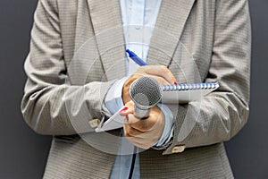 Female journalist at media event or press conference, writing notes, holding microphone