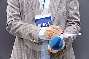 Female journalist at news conference or media event, writing notes, holding microphone