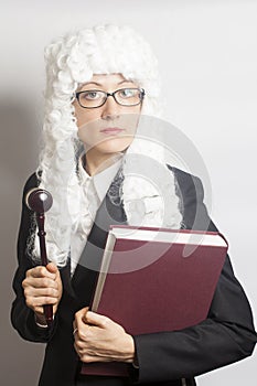 Female judge wearing a wig and Back mantle with eyeglasses holding judge gavel and book