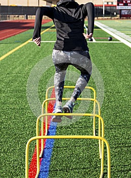 Female jumping over mini hurdles from behin