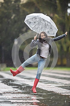 Female jumps from joy on a rainy day with an umbrella and red polka dot rain boots