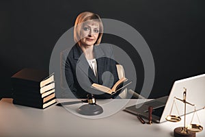 Female jurist isolated at the dark background. Books and gavel with justice scales. photo