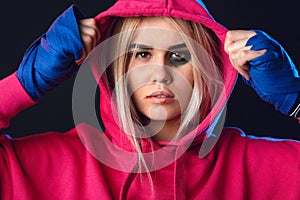 Female kick boxer with bruise dressed in pink hoodie and boxing bandages.