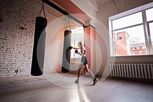 Female kickboxer hitting punching bag while dust particles flies in sunflare light background.