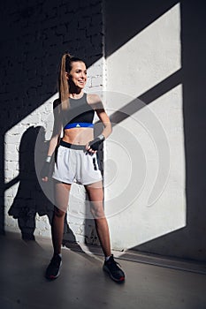 Female kickboxer standing in a boxing studio while dust particles flies in sunflare light background.