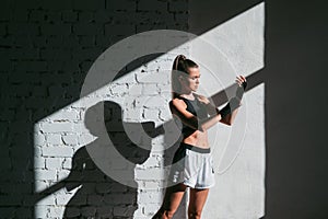 Female kickboxer standing in a boxing studio while dust particles flies in sunflare light background.