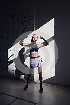 Female kickboxer standing in a boxing studio while dust particles flies in sunflare light background.