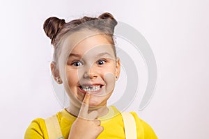 Female kid with opened mouth pointing at missing front baby tooth with finger smiling excitedly in yellow t-shirt on