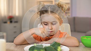 Female kid refusing to eat broccoli, throwing vegetable away, vitamin nutrition