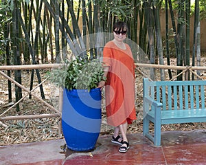 Female Korean tourist standing next to a blue pot with Ruscus aculeatus in the Jardin Majorelle in Marrakesh, Morocco.