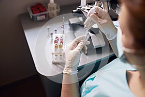 Female lab tech takes sample from test tube to research material at workplace with modern equipment