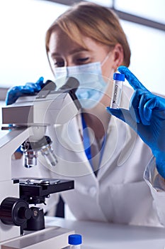 Female Lab Worker Wearing PPE Researching Covid-19 Omicron Variant In Laboratory With Microscope