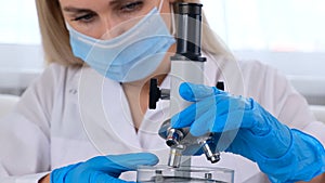 Female laboratory assistant analyzes samples using a microscope while working at a table in a laboratory, doing research