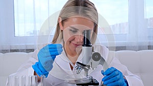 Female laboratory assistant analyzes samples using a microscope while working at a table in a laboratory, doing research