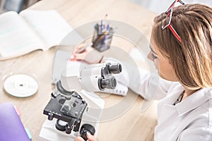 Female laboratory technician writing down observations from work with a microscope